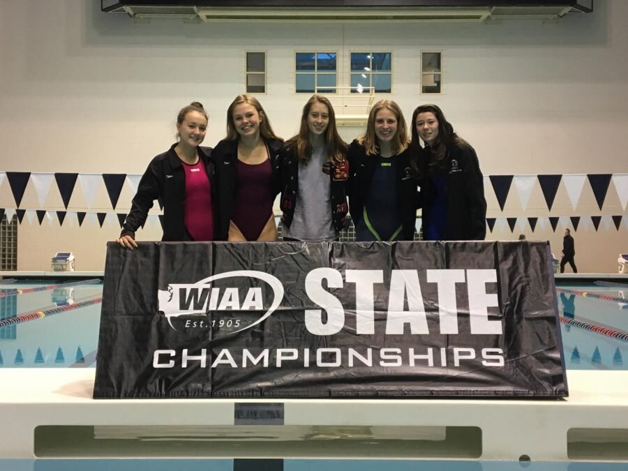 From left to right: Addy Keenan (10), Cassidy Wilton (12) (alt.), Hanna Parker (12), Olivia Gabanek (12), Corinne Pickering (9) pose in front of State Champions banner at the King County aquatic center. (Ella Haskens)