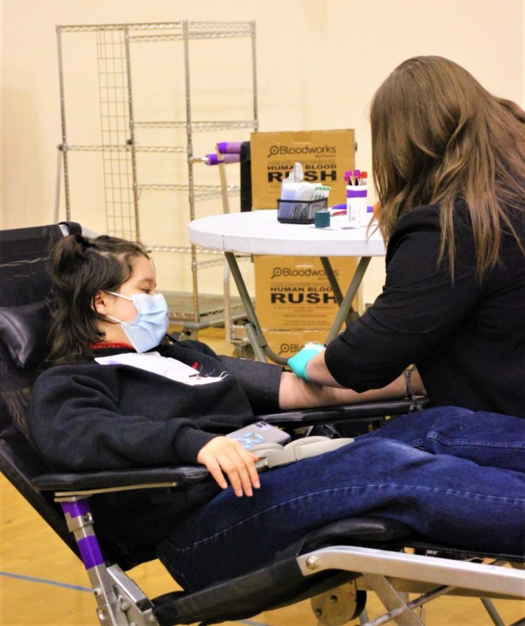 Izzy Kim (12) sits back as a Bloodworks Northwest employee prepares her arm for blood donation.