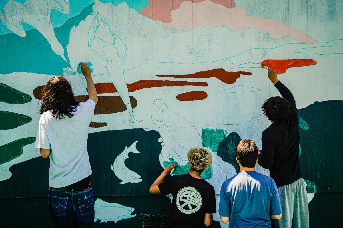 Art Survey students, with paintbrushes in hand, crowd around the exterior wall of Portable 202.